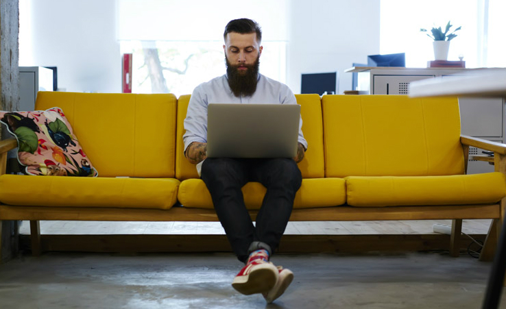Man sitting on a yellow sofa with a laptop
